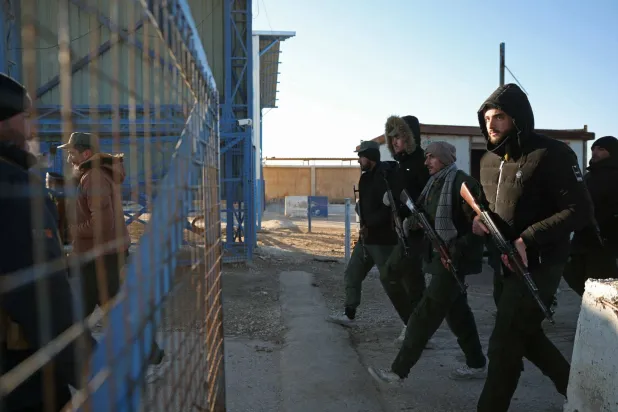 TOPSHOT - Members of Syrian security forces march through the entrance of the Al-Hol camp in the desert region of Hasakeh province on January 21, 2026. (Photo by OMAR HAJ KADOUR / AFP)