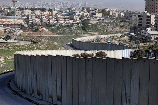 صورة لمستوطنة بسغات زئيف الإسرائيلية (يسار) التي بنيت في ضاحية من ضواحي القدس الشرقية ذات الأغلبية العربية خلف جدار الفصل الإسرائيلي في 16 فبراير 2026 (أ.ف.ب)