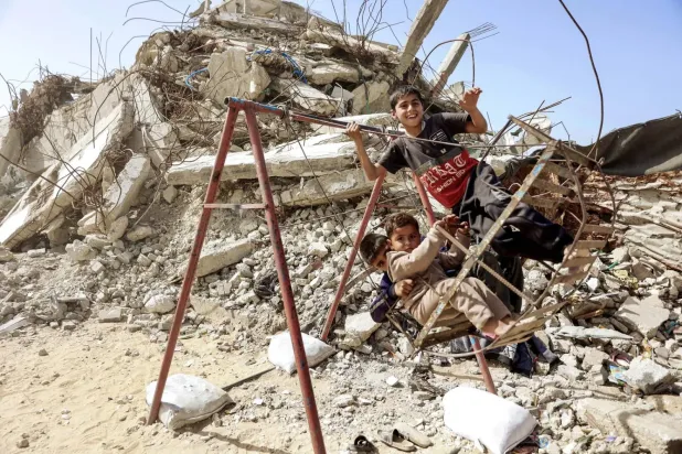 Gazze şehrinde yıkılmış bir binanın kalıntıları arasında oyun oynayan çocuklar (AFP)