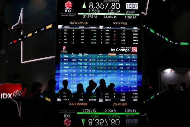 أشخاص يمرون أمام لوحة إلكترونية تعرض حركة الأسهم في بورصة إندونيسيا (رويترز)