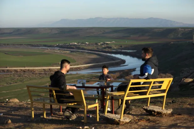 People sit outdoors surrounded by nature, with the Tigris river flowing in the background, following a long atmospheric depression, near the Syrian-Turkish border in Derik, Syria, February 16, 2026 REUTERS/Orhan Qereman

