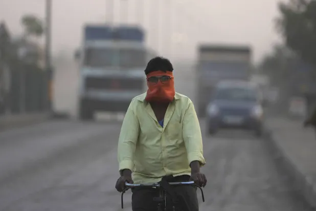 رجل يغطي وجهه في أثناء ركوبه دراجة وسط الغبار والتلوث في الهند (أ.ب)