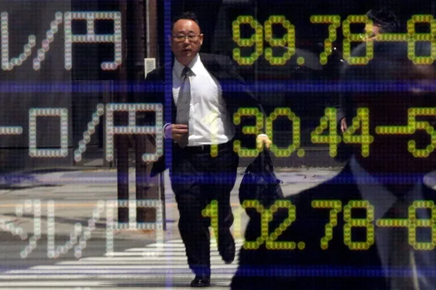 رجل يركض على ممر للمشاة ينعكس على لوحة إلكترونية تعرض أسعار الصرف خارج مكتب وساطة في طوكيو (رويترز)