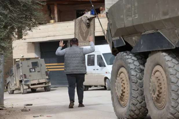 رجل فلسطيني يرفع يديه أثناء اعتقاله من قبل القوات الإسرائيلية خلال مداهمة عسكرية في جنين بالضفة الغربية (إ.ب.أ)