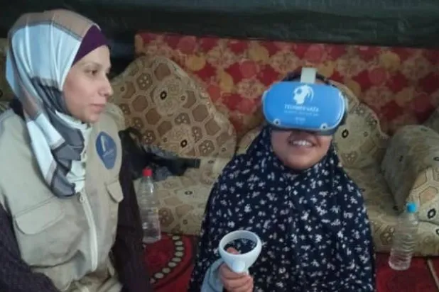 طفلة تتابع مشاهد افتراضية في غزة (يمين) مع إحدى العاملات في مشروع «تك ميد غزة» (صفحة المشروع على «إنستغرام»)