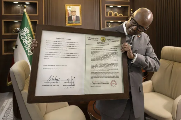 وزير رئاسة جمهورية أرض الصومال خضر حسين عبدي يقف أمام شهادة مؤطرة تحتوي على إعلان موقع من إسرائيل بالاعتراف بأرض الصومال كدولة (أ.ف.ب)