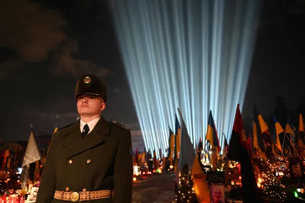 A Ukrainian Honor Guard stands as a symbolic illumination entitled "Rays of Memory" is projected over the graves of Ukrainian soldiers who died in the war with Russia, at Lychakiv Military Cemetery in Lviv on February 23, 2026, ahead of the fourth anniversary of Russia's invasion of Ukraine. (AFP) 