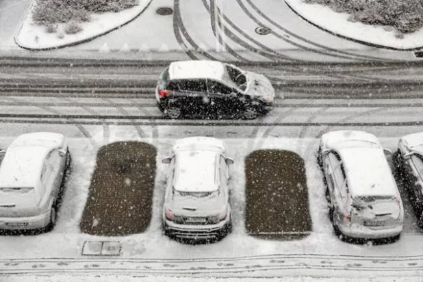 سيارة تمر بجانب مركبات أخرى متوقفة مغطاة بالثلوج في موقف بريشوف في بولندا (رويترز)