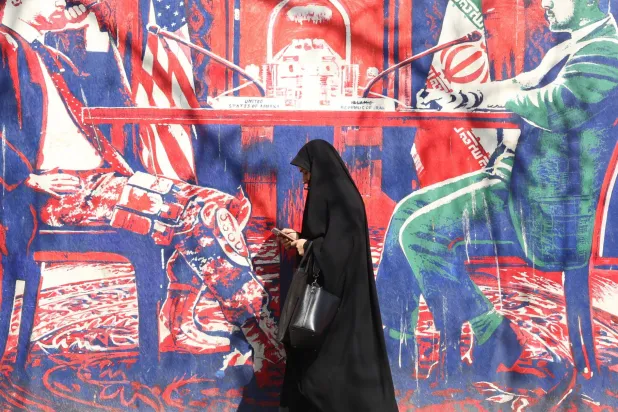A veiled Iranian woman walks past an anti-US mural in Tehran, Iran, 23 February 2026. (EPA)