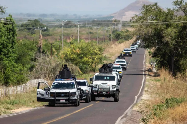 Members of the Civil Guard of Michoacan patrol a highway supported by armored vehicles after a wave of violence in the town of Aguililla, in Tierra Caliente, Mexico, on February 24, 2026. (Photo by Enrique Castro / AFP)