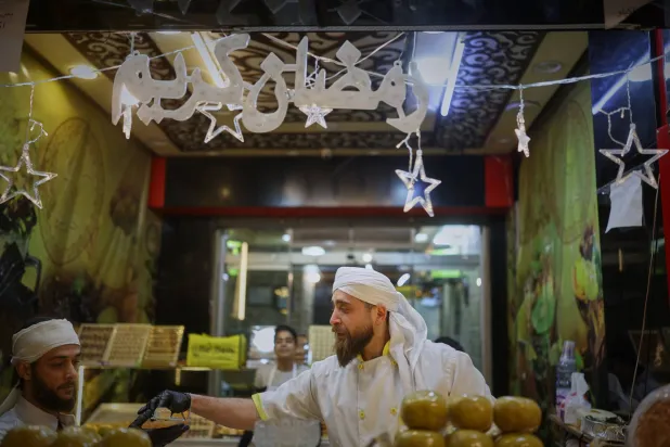 بائع متجول يعتني بكشكه المضاء جيداً والمليء بحلويات رمضان في دمشق (أ.ب)