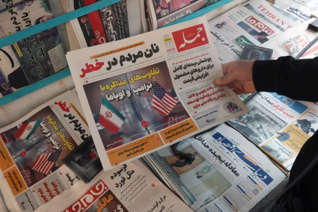 رجل إيراني يحمل نسخة من صحيفة «جومله» الإيرانية اليومية تحمل عنواناً باللغة الفارسية: «الاختلافات بين التفاوض مع دونالد ترمب وباراك أوباما» (إ.ب.أ)