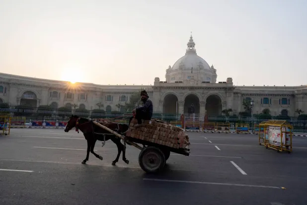 رجل على عربة يجرها حصان يمر في أحد شوارع مدينة لوكنو بولاية براديش الهندية (أ.ب)