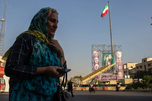 إيرانية تمر أمام صاروخ محلي الصنع من طراز «خيبر شكن» ولافتات عليها صور للمرشد الإيراني علي خامنئي (وسط) وقادة القوات المسلحة الراحلين الذين قُتلوا إثر غارة إسرائيلية بشهر يونيو بميدان بهارستان في طهران (نيويورك تايمز)