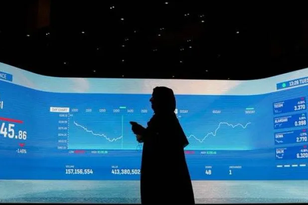 إماراتية تسير إلى جانب شاشة تداول في بورصة دبي (رويترز)
