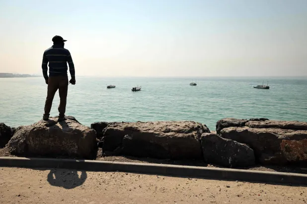صياد ينظر نحو الأفق بميناء الصيد في العقير على مضيق هرمز بإمارة رأس الخيمة الشمالية (أ.ف.ب)