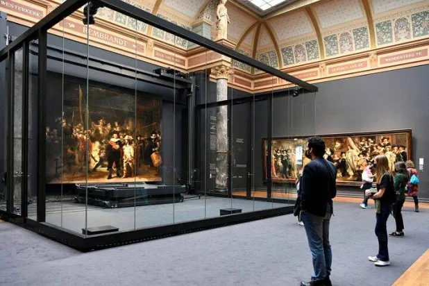 Poeple look at Rembrandt's famed Night Watch, which is back on display in what researchers say in its original size, with missing parts temporarily restored in an exhibition aided by artificial intelligence, at Rijksmuseum in Amsterdam, Netherlands June 23, 2021. REUTERS/Piroschka van de Wouw/File Photo