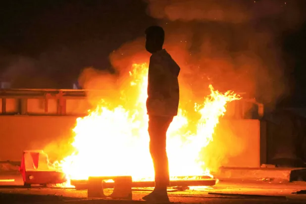 شخص قرب حريق بينما يشتبك متظاهرون مع قوات الأمن العراقية خلال محاولتهم الاقتراب من السفارة الأميركية في بغداد (أ.ف.ب)