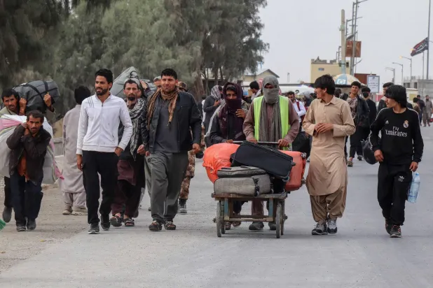 مواطنون أفغان بالقرب من جسر الحرير بعد عودتهم من إيران عند معبر حدودي (أ.ف.ب)