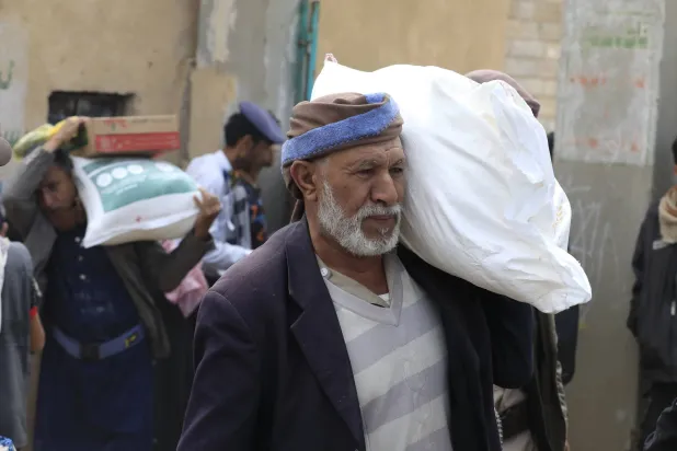 رجل يحمل جوال مساعدات غذائية في منطقة بغرب اليمن (إ.ب.أ)