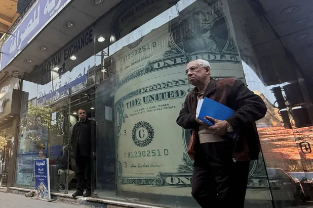 رجل مصري يمر أمام شاشة عرض لعملة الدولار الأميركي (رويترز)