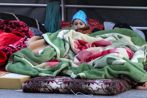 A boy looks on while lying under a blanket alongside family belongings in a makeshift encampment along the waterfront in Beirut on March 10, 2026, as civilians who fled the city's southern suburbs due to Israeli bombardment remain displaced. (AFP)