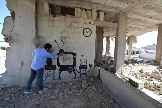 «بانكسي السوري» يشير إلى جدارية رسمها على جدار مبنى قبل فراره من داريا عام 2016 (أ.ف.ب)