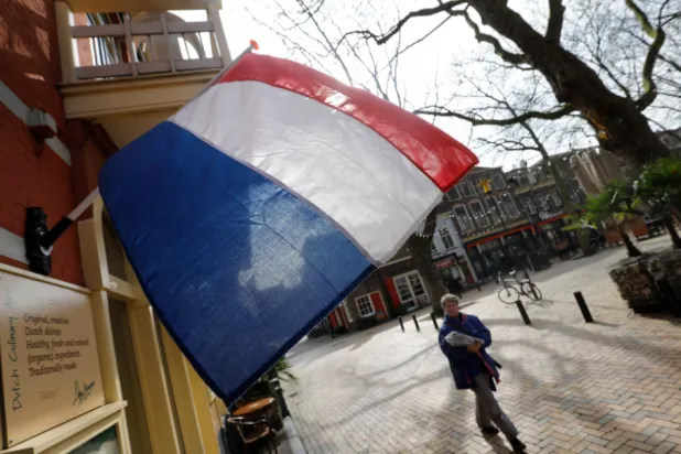 A woman walks past a national flag, the day before a general election, in Delft, Netherlands, March 14, 2017. REUTERS/Yves Herman 