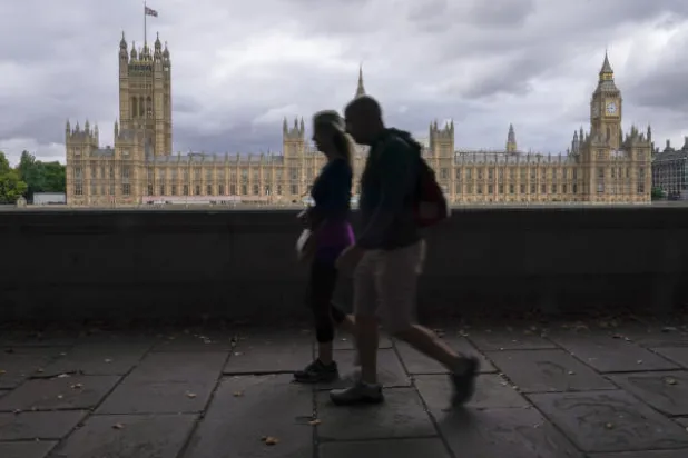 مشاة يسيرون على الضفة الجنوبية لنهر التايمز خلفها قصر وستمنستر في لندن (أ.ف)