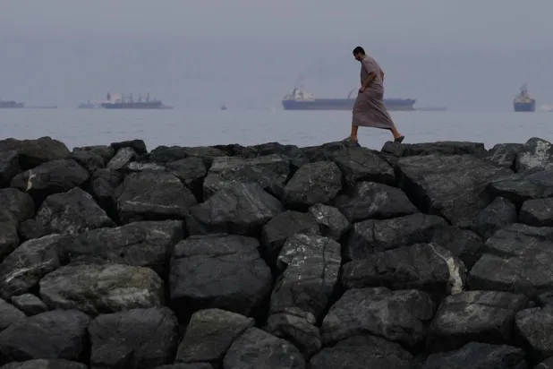 A man walks along the shore as oil tankers and cargo ships line up in the Strait of Hormuz, seen from Khor Fakkan, United Arab Emirates, Wednesday, March 11, 2026. (AP)