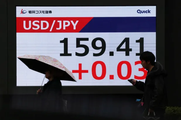 مشاة يمرون أمام شاشة تعرض حركة الين الياباني مقابل الدولار في وسط العاصمة اليابانية طوكيو (رويترز)