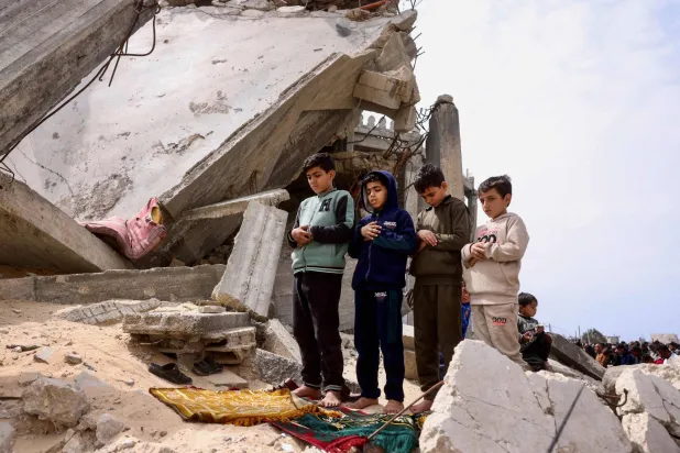 أطفال فلسطينيون يشاركون في صلاة الجمعة فوق أنقاض مسجد الطالباني الذي دمره القصف الإسرائيلي خلال الحرب في خان يونس جنوب قطاع غزة (أ.ف.ب)