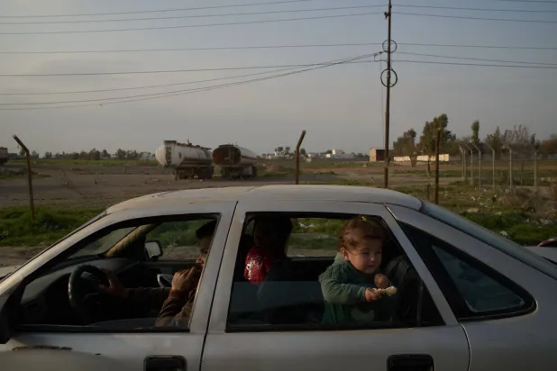 رجل برفقة أطفاله على طريق يمر بجانب شاحنات في ضواحي أربيل شمال العراق (أ.ب)