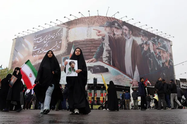 نساء إيرانيات يمشين أمام لوحة تحمل صور المرشد مجتبى خامنئي وقادة عسكريين خلال مسيرة في طهران (إ.ب.أ)