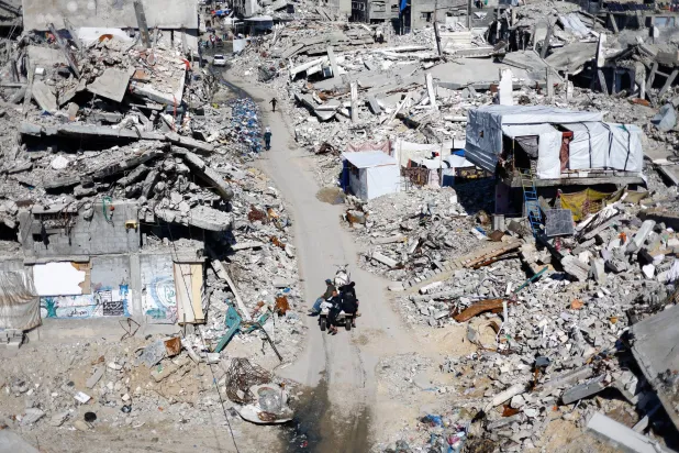 فلسطينيون يمرون أمام أنقاض المباني السكنية التي دُمرتها إسرائيل في جباليا شمال قطاع غزة (رويترز)