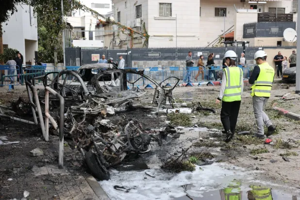 Acil durum hizmetinden iki personel, dün Tel Aviv'de İran'ın balistik füzesinin düşürülmesi sonucu yanan araçları inceliyor (EPA)