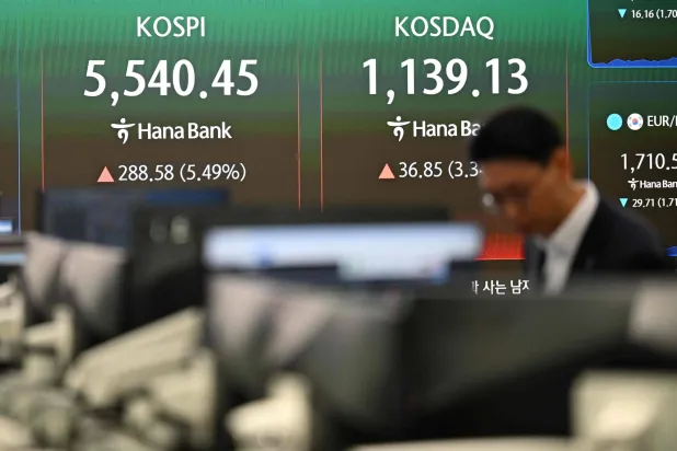 متعامل عملات يراقب أسعار الصرف أمام شاشة تُظهر مؤشري «كوسبي» و«كوسداك» بغرفة تداول ببنك هانا في سيول (أ.ف.ب)