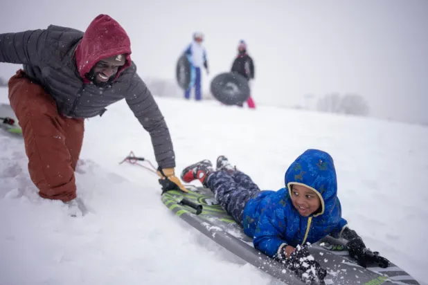Ogo Akpati and his son Brycson Akpati, 3, braved the strong winds and had fun sliding down a hill in Central Park Sunday, March 15,2026 in Brooklyn Park, MN. (Jerry Holt/Minnesota Star Tribune via AP)
