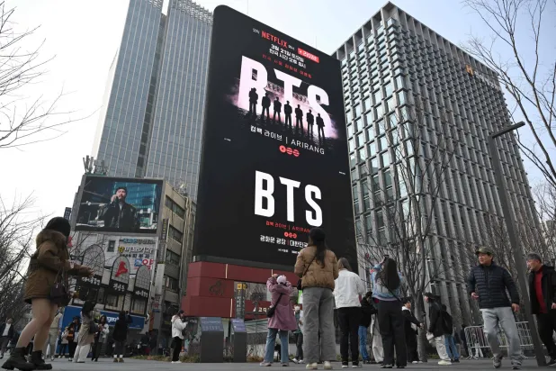 People walk past a billboard promoting a comeback concert of K-pop boy group BTS at Gwanghwamun Square in Seoul on March 17, 2026. (AFP)