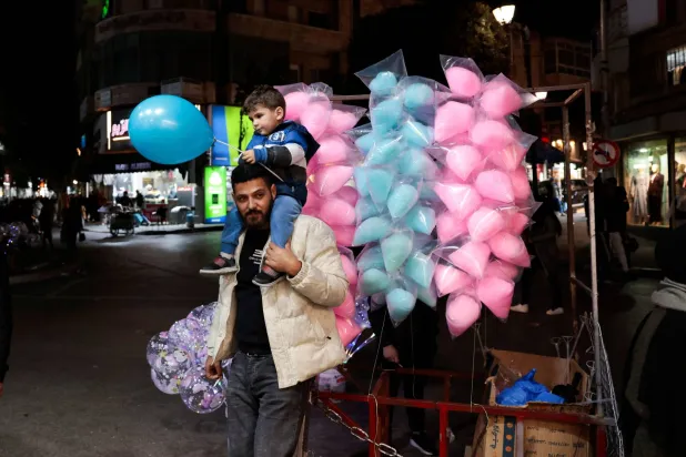 فلسطيني يحمل ابنه يوم الثلاثاء في رام الله بالضفة الغربية قبل حلول عيد الفطر  (رويترز)