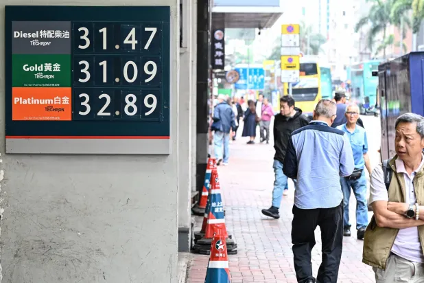 مشاة يمرون أمام لوحة تعرض أسعار الوقود في محطة بمدينة هونغ كونغ الصينية (أ.ف.ب)