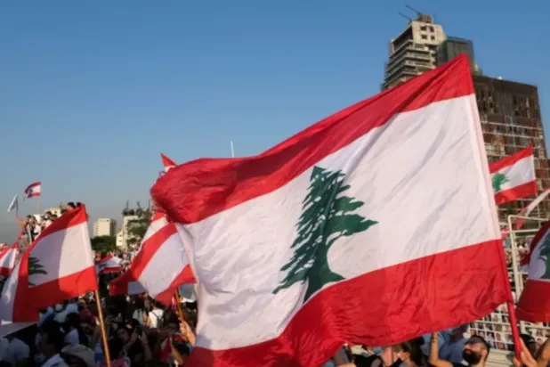People carry national flags as they hold a moment of silence marking the one-year anniversary of Beirut's port blast, near the site of the explosion in Beirut, Lebanon August 4, 2021. REUTERS/Emilie Madi 