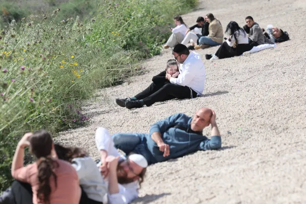 إسرائيلي يحمل ابنته بينما يتبع هو وآخرون تعليمات الجيش الإسرائيلي بالاستلقاء على الأرض مع انطلاق صفارات الإنذار في تل أبيب يوم 20 مارس 2026 (إ.ب.أ)