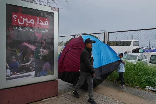 نازح من جنوب لبنان إلى وسط بيروت وإلى جانبه لوحة إعلامية تتضمن شعاراً مناهضاً للحرب (أ.ب)