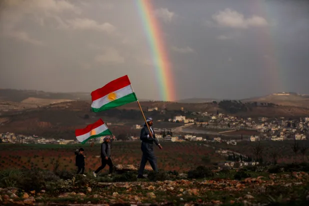 سوريون أكراد يحملون أعلاماً كردية استعداداً للاحتفال بـ«النوروز» في عفرين بمدينة حلب الجمعة (رويترز)