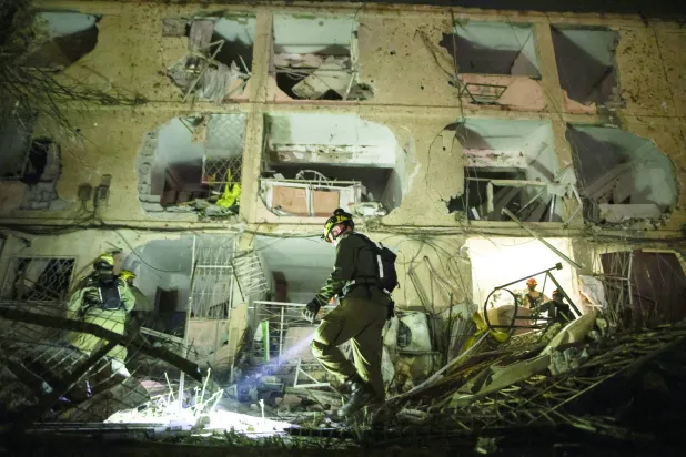 جندي إسرائيلي يستخدم مصباحاً يدوياً لتفقد الأضرار التي خلفها صاروخ إيراني في ديمونة (رويترز) 