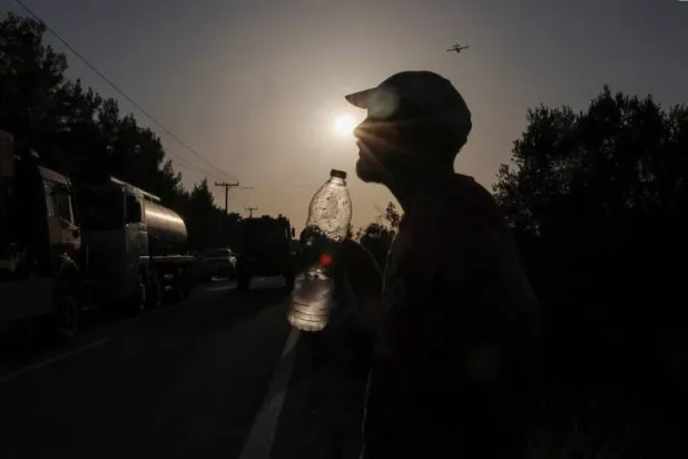 A volunteer holds a bottle of water as a wildfire burns in the village of Vati, on the island of Rhodes, Greece, July 26, 2023. REUTERS/Nicolas Economou/File photo