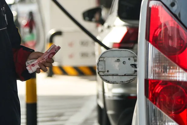 موظف يحمل أوراقاً نقدية من اليوان الصيني بجوار غطاء مفتوح لخزان وقود سيارة في محطة وقود في بكين (رويترز)