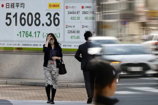 Tokyo Borsası’nın hisse senedi endeks panosunun önünden geçen insanlar (EPA)