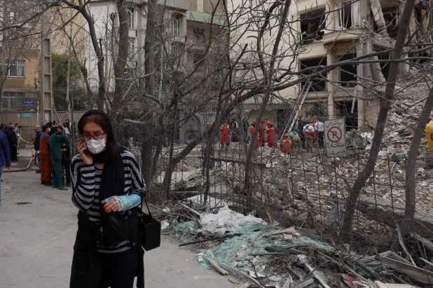 سيدة إيرانية مصابة تسير بجانب مبنى تضرر جراء الغارات الأميركية - الإسرائيلية شمال طهران أمس (إ.ب.أ)